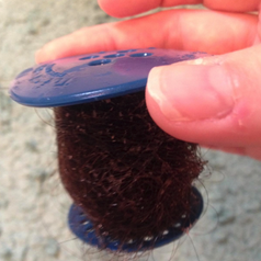 a reviewer's hand holding the tub drainer which has hair wrapped around it that didn't go down the drain