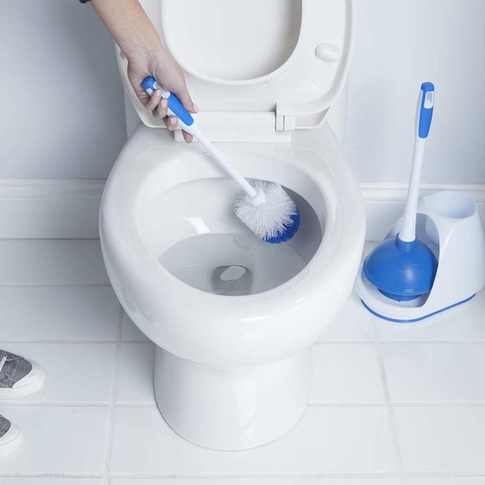 model&#x27;s hand putting the toilet scrubber into the tub and the holder sitting beside the tub with the plunger also in it