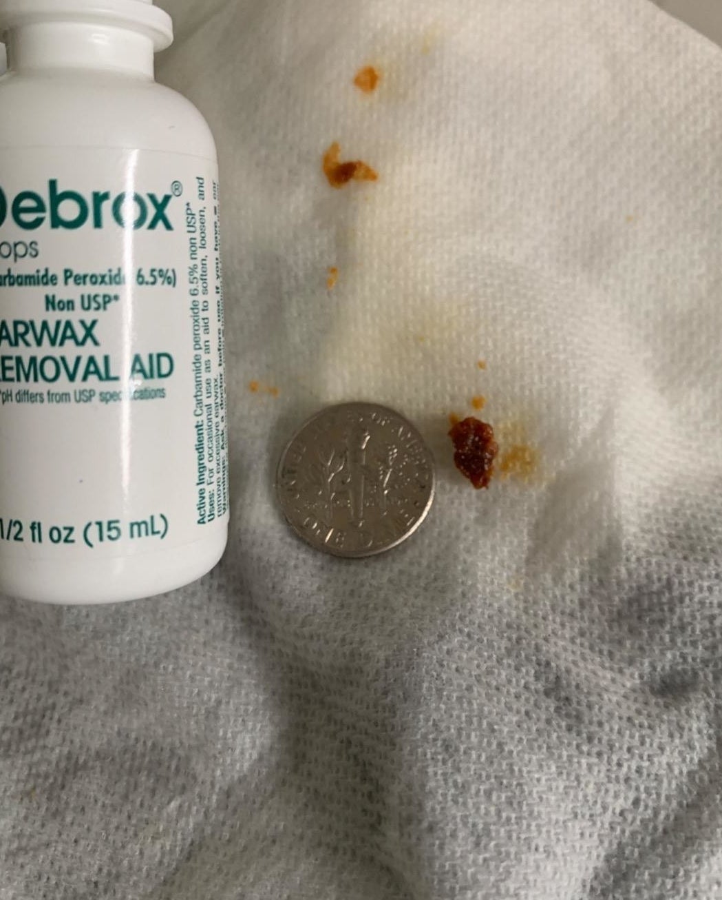 A tissue with clumps of earwax next to a dime for size as well as the container of drops