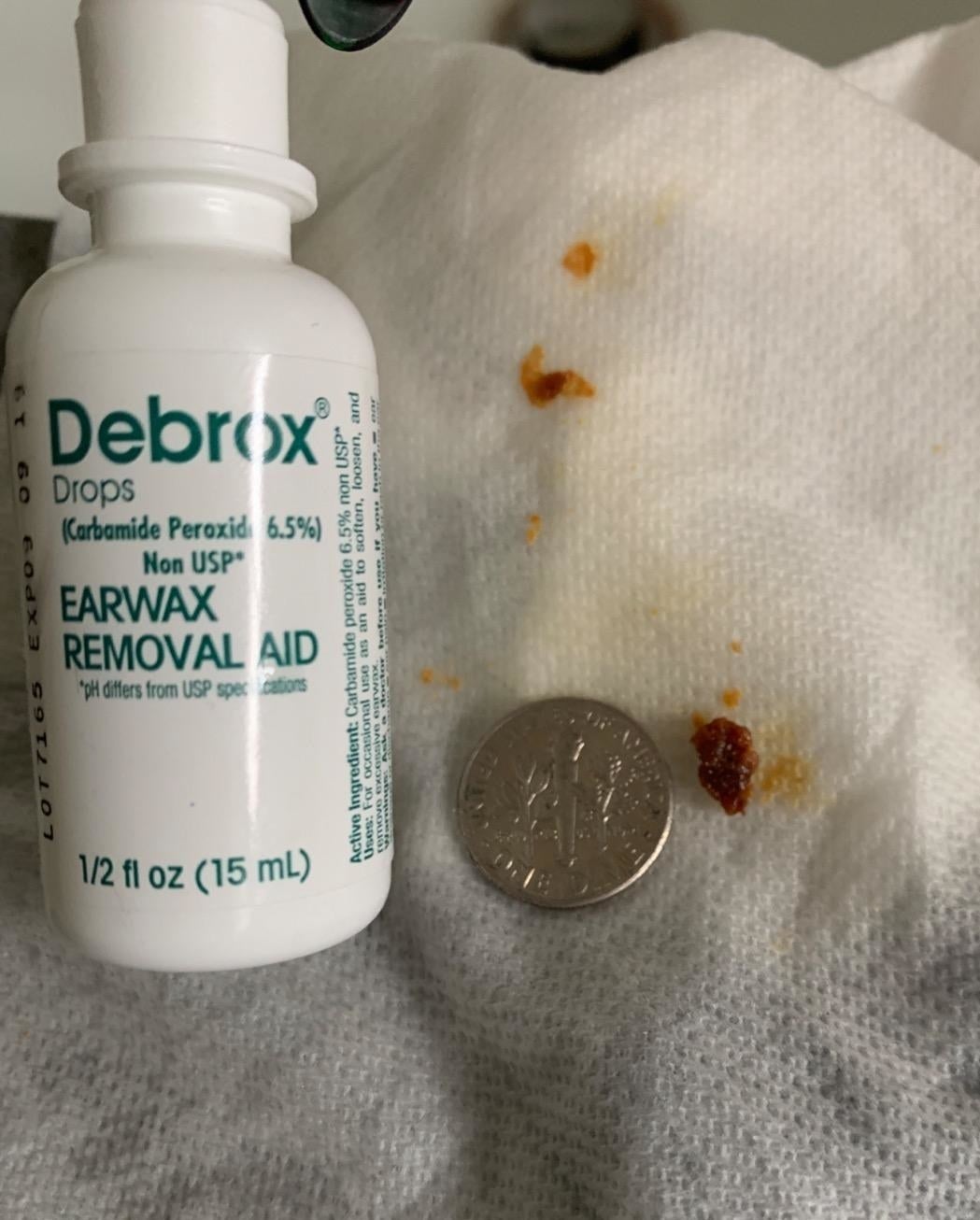 A tissue with clumps of earwax next to a dime for size as well as the container of drops