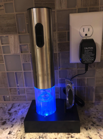 the wine opener sitting on a charging deck which is plugged into an outlet on a counter