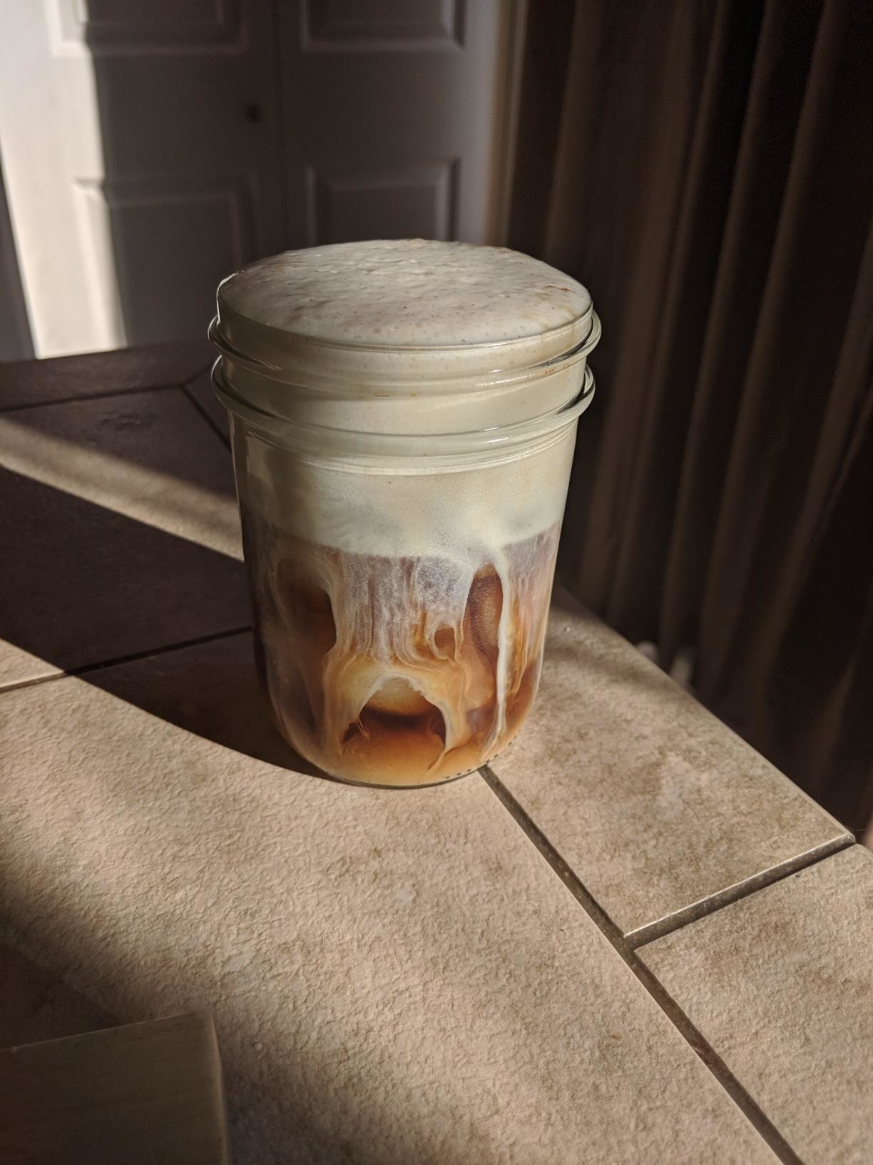 A mason jar filled with iced coffee and foamed milk