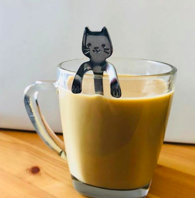 reviewer pic of a cat shaped spoon in a coffee mug with paws resting on side of mug