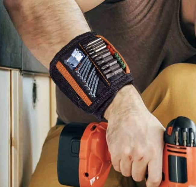 model wearing the band with screws and bits sticking to it as he holds a drill
