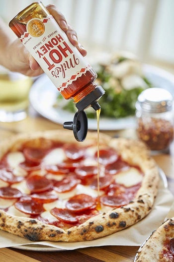 A person pouring the hot honey over pepperoni pizza
