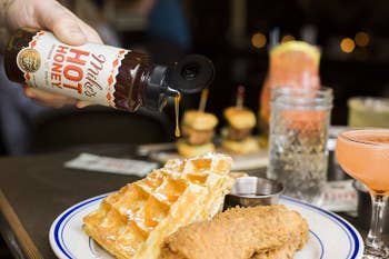 A person pouring the hot honey over a plate of chicken and waffles