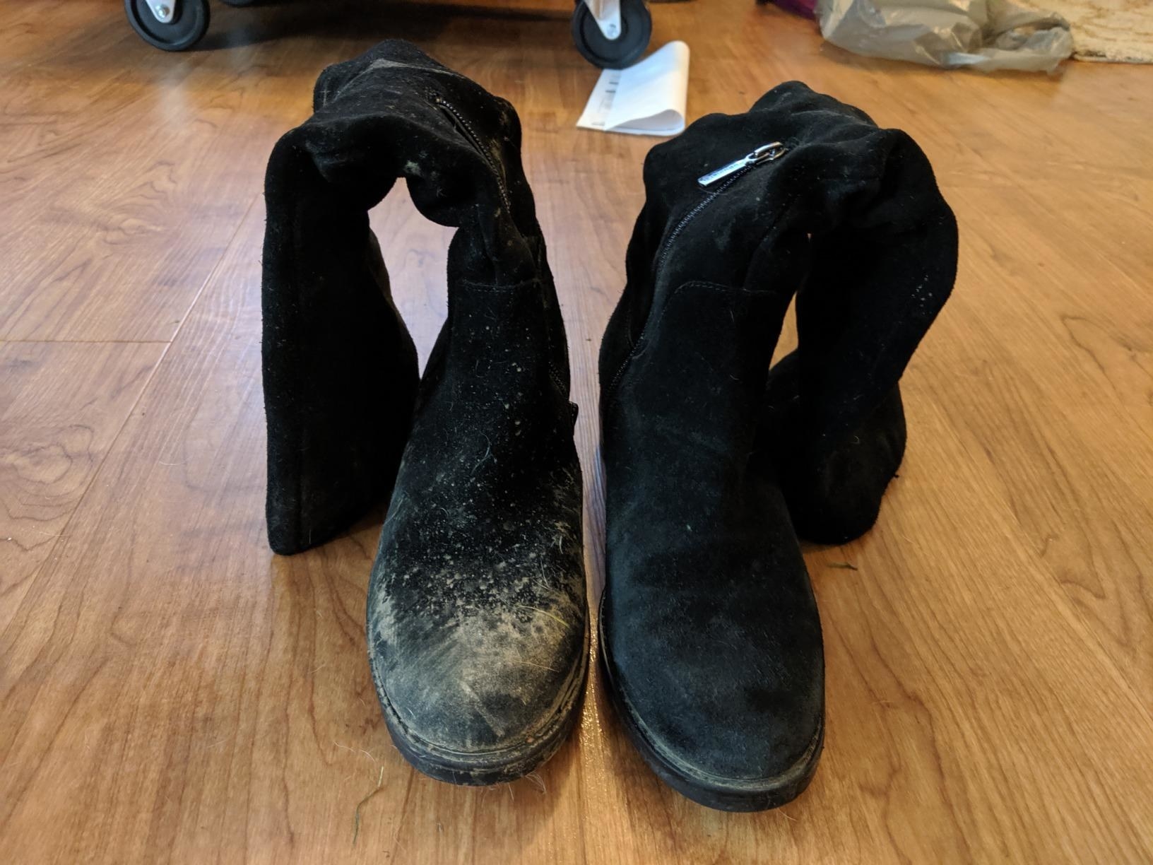 A reviewer&#x27;s black suede boots: the left covered in light brown dirt, the right completely clean and new-looking
