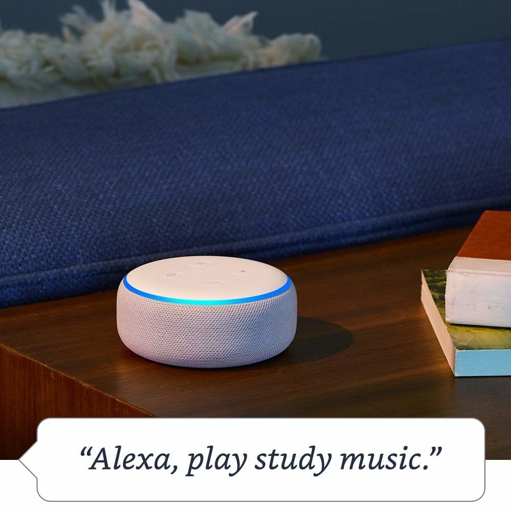 A round white Echo Dot ringed with a blue light sits on a wooden table with the phrase &quot;Alexa, play study music.&quot; in a speech bubble below it. 