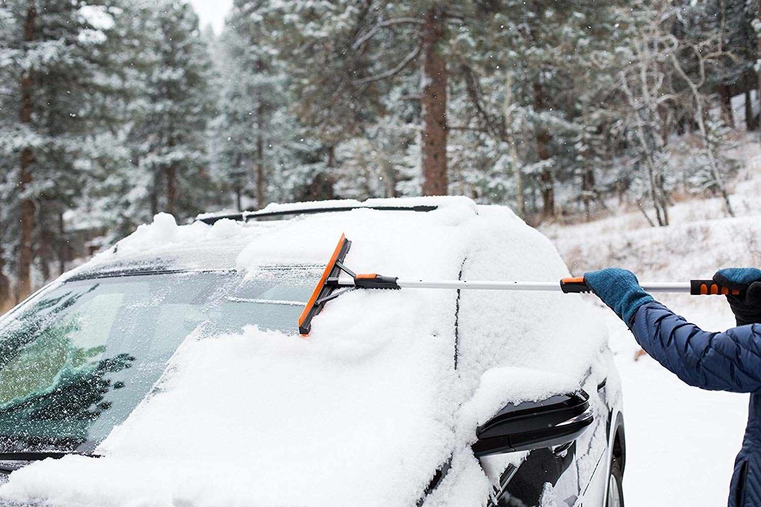 Person scraping snow off windshield with extendable squeegee pole 