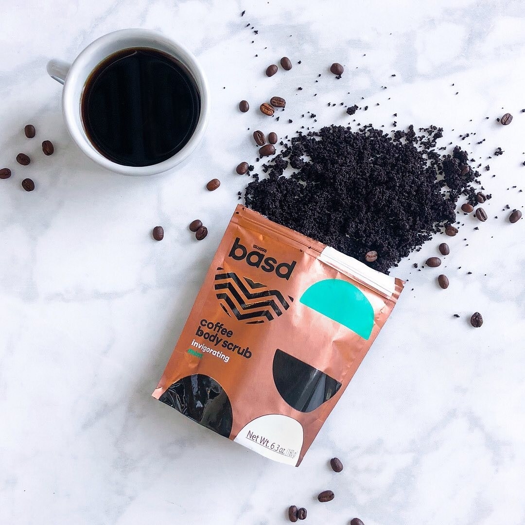 A bag of coffee body scrub lying half open on a table with coffee beans mixed in