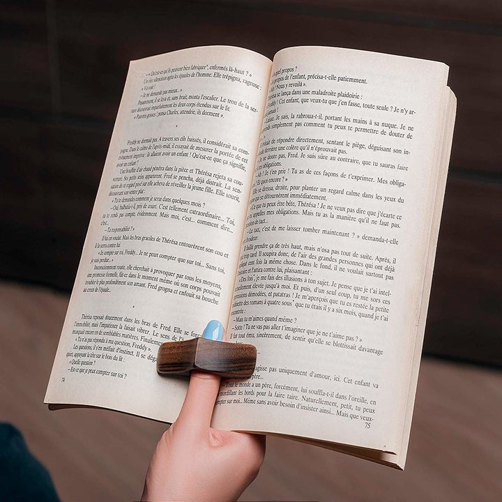 A person reading a book with a large diamond-shaped wooden ring over their thumb 