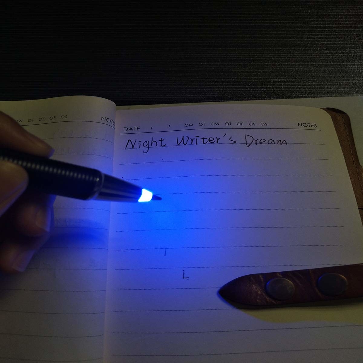 Image of a hand writing with a light-up pen in the dark.
