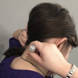 This a close-up of BuzzFeed editor Katy Herman applying the essential oil stick to the back of her neck while she holds her brown hair to the side.