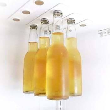six-pack of bottled beer hanging from magnets that are attached to fridge shelf 