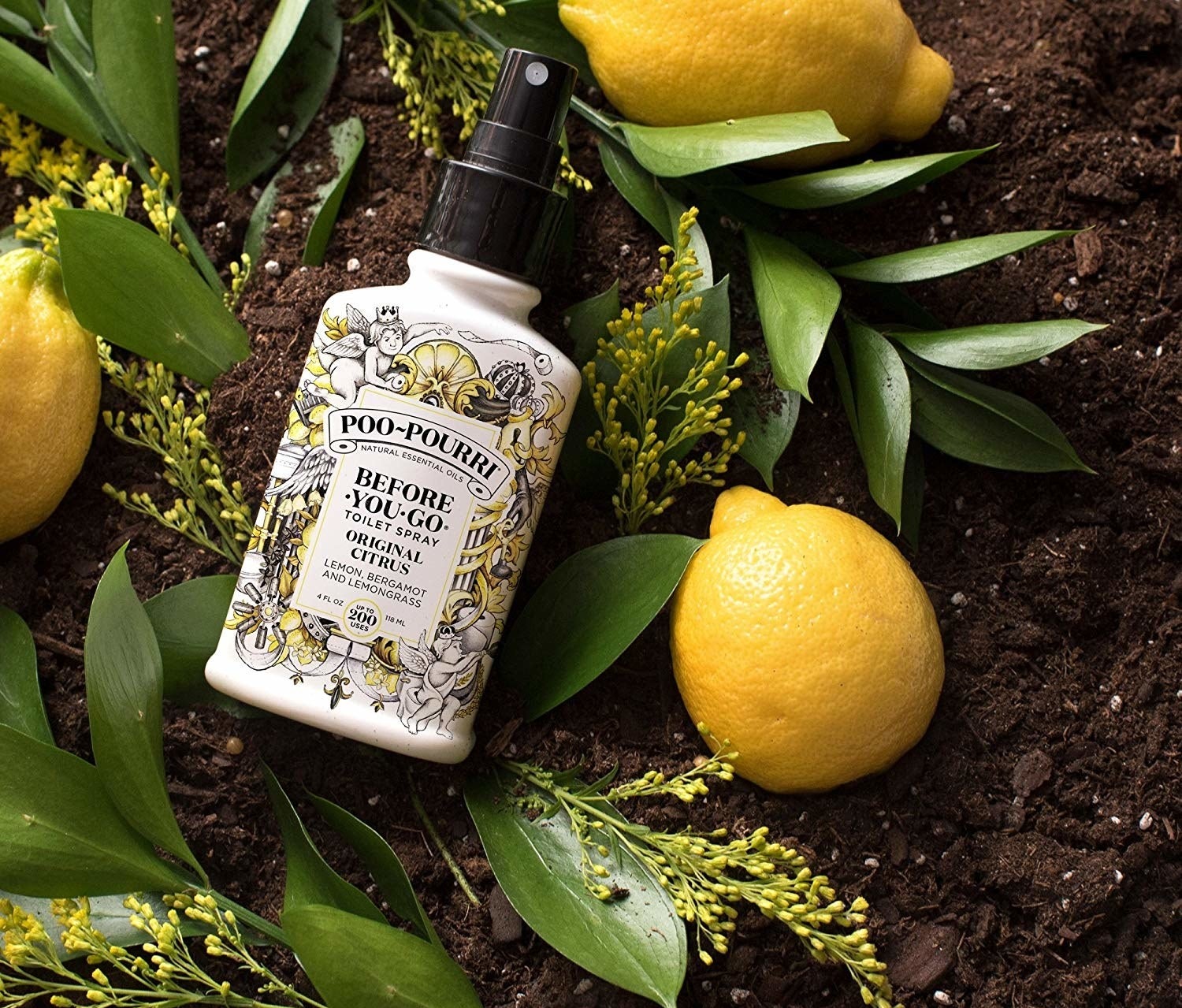 A bottle of lemon-scented toilet spray placed artfully on soil with lemons and leaves around it