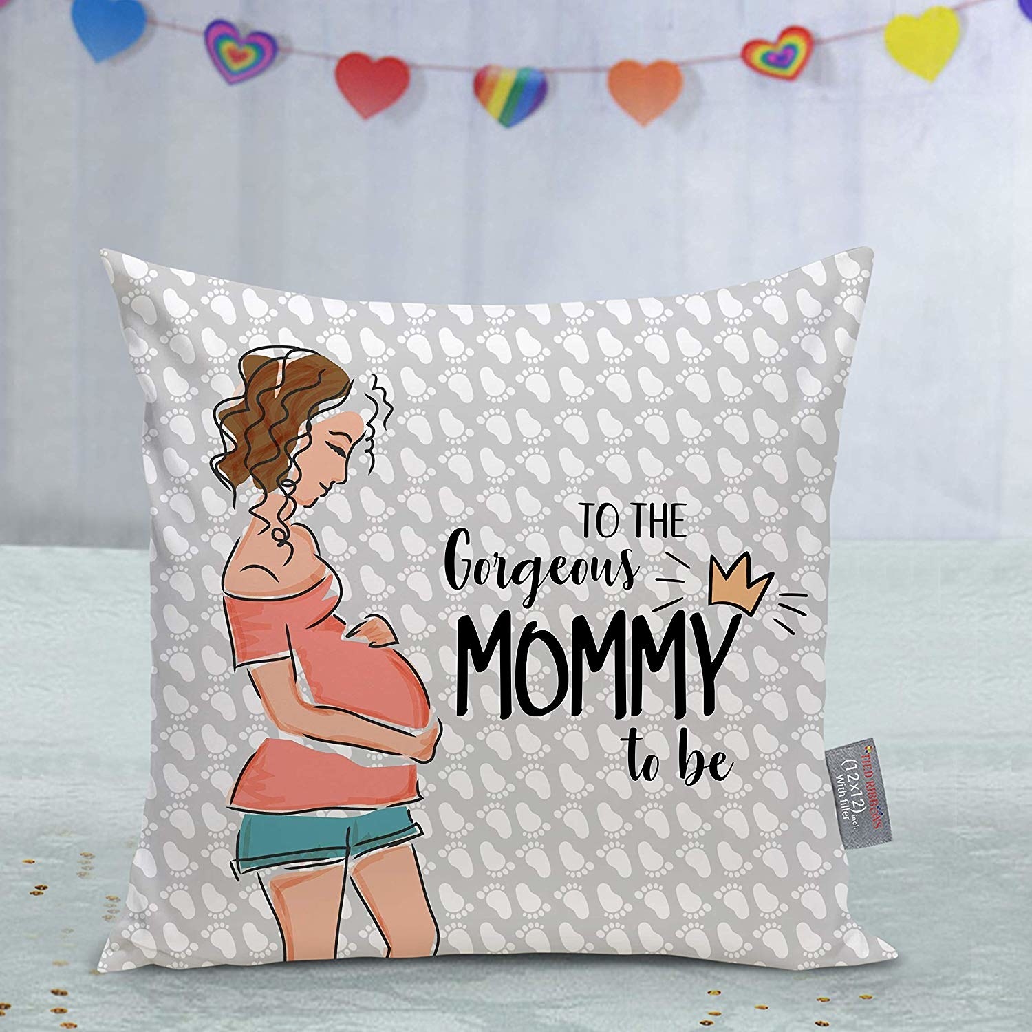 A grey cushion patterned with tiny white footprints. It has a print of a pregnant lady with the words, &quot;To the gorgeous mommy to be&quot;.