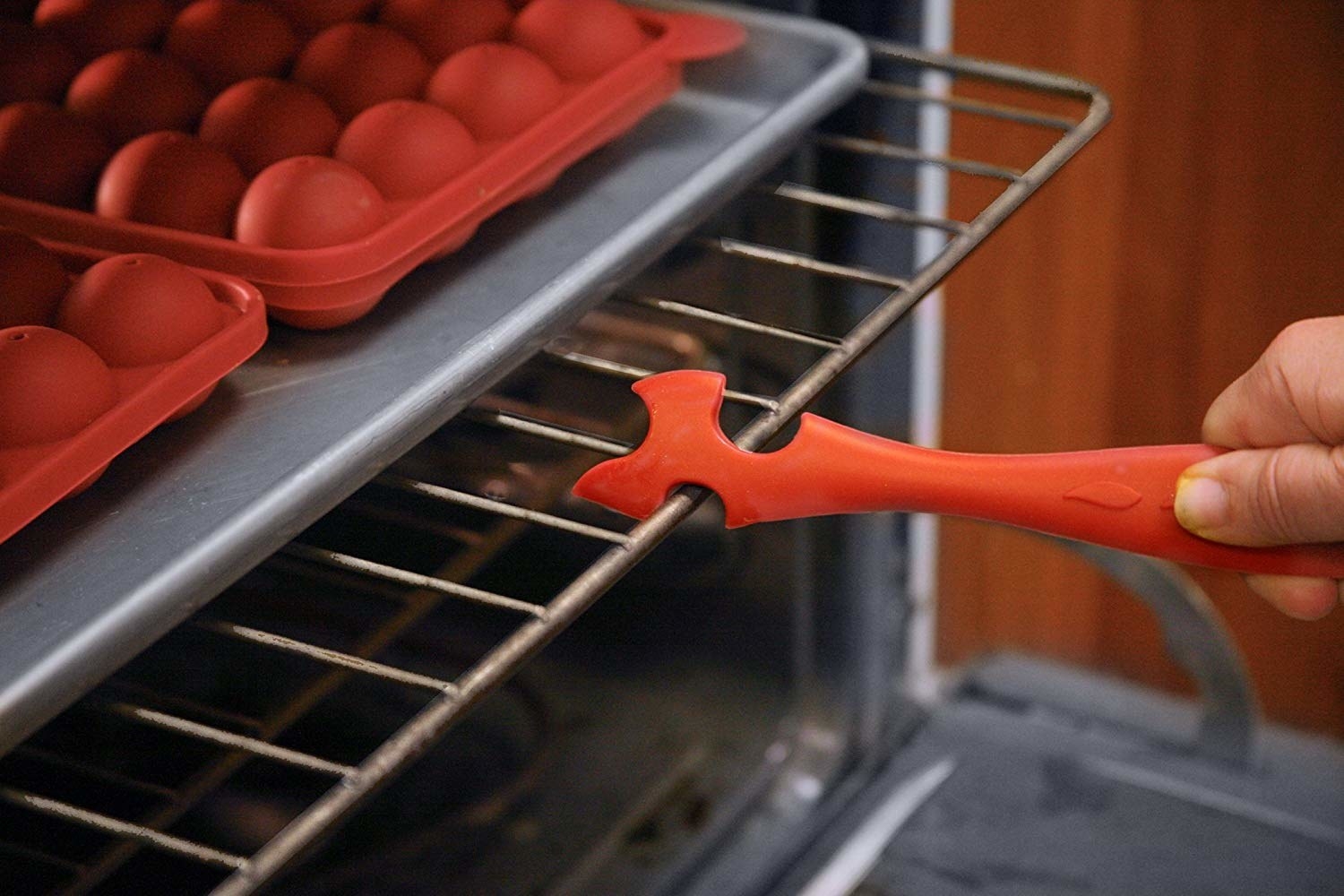 A person using a small long silicone hook to pull an oven rack out of the oven