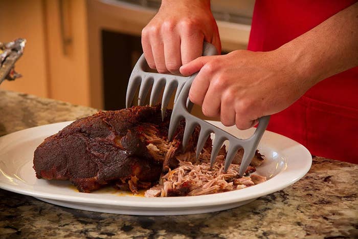 A person using metal claws to shred meat on a plate