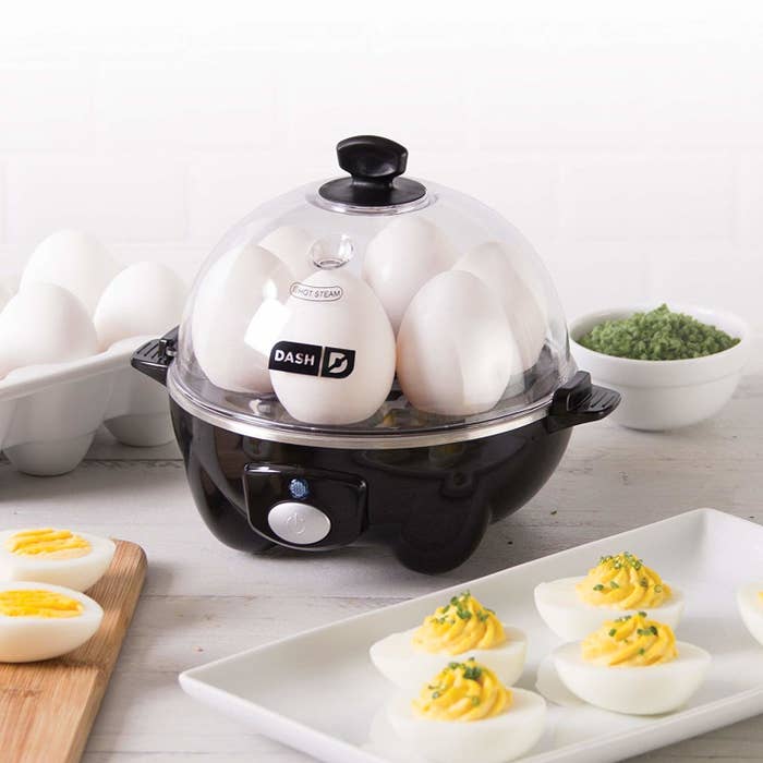 A small round electronic egg cooker with six eggs on the base and a lid over top