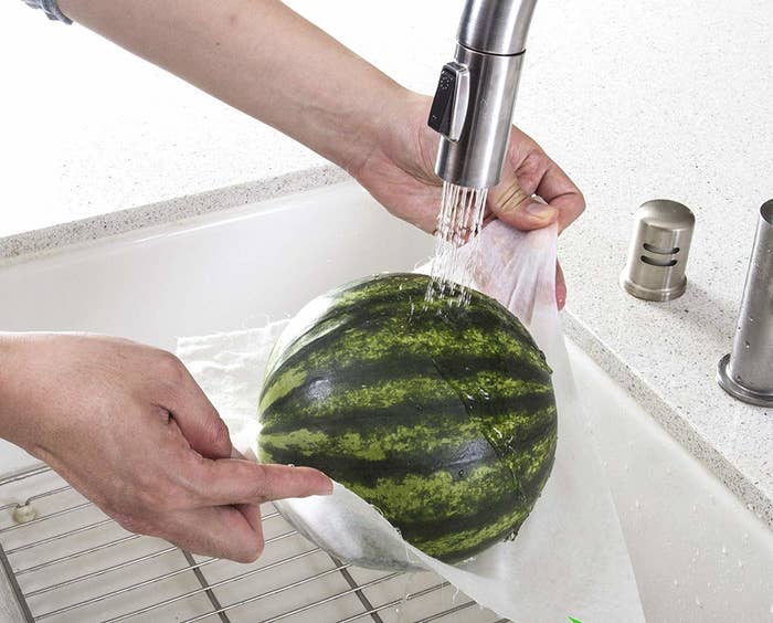 small watermelon held up with wet paper towel under faucet 
