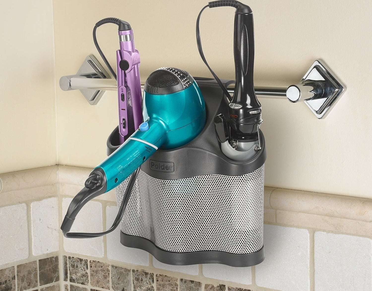 A plastic storage organizer with three slots hanging from a towel rack in the bathroom In one slot is a hair straightener, in another is hair dryer and in the last one is a curling iron