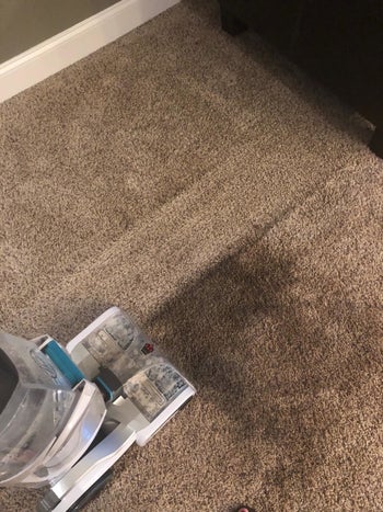 Reviewer using the Hoover on their carpet and you can clearly see the clean line of the carpet next to the mess it's cleaning up