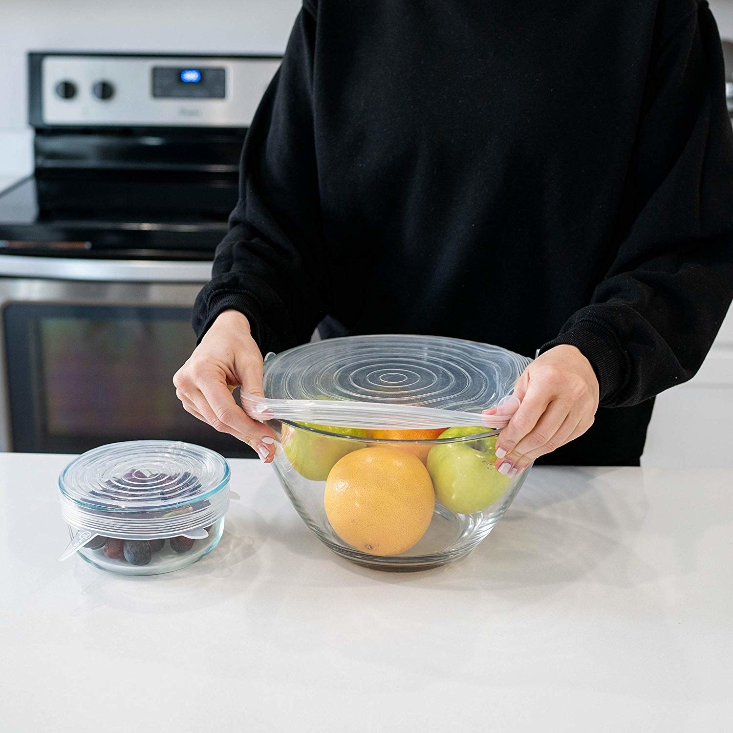 Person covering fruit bowl with adjustable silicone lid 