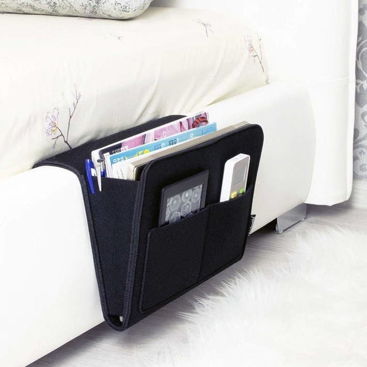 The caddy attached to the side of a bed, holding a remote, tablet, and magazines