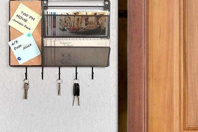 The black mesh mall sorter has a cork board, two mail slots, and five key hooks 