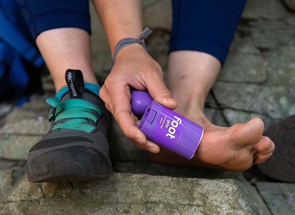 A person applying the product, which looks like it has a deodorant-like packaging, to their foot