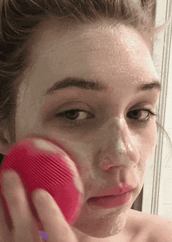 a gif of a buzzfeed editor using the pink cleaning brush to soap up their face
