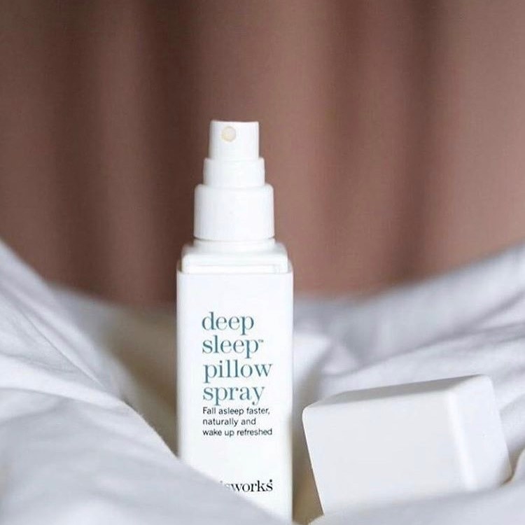 A bottle of the spray nestled into the bed sheets