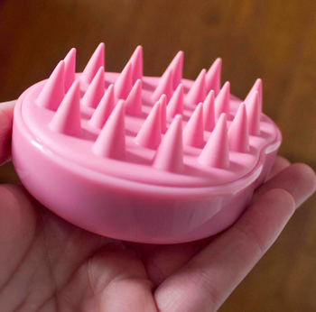 Pink shampoo brush being held upside-down in hand 