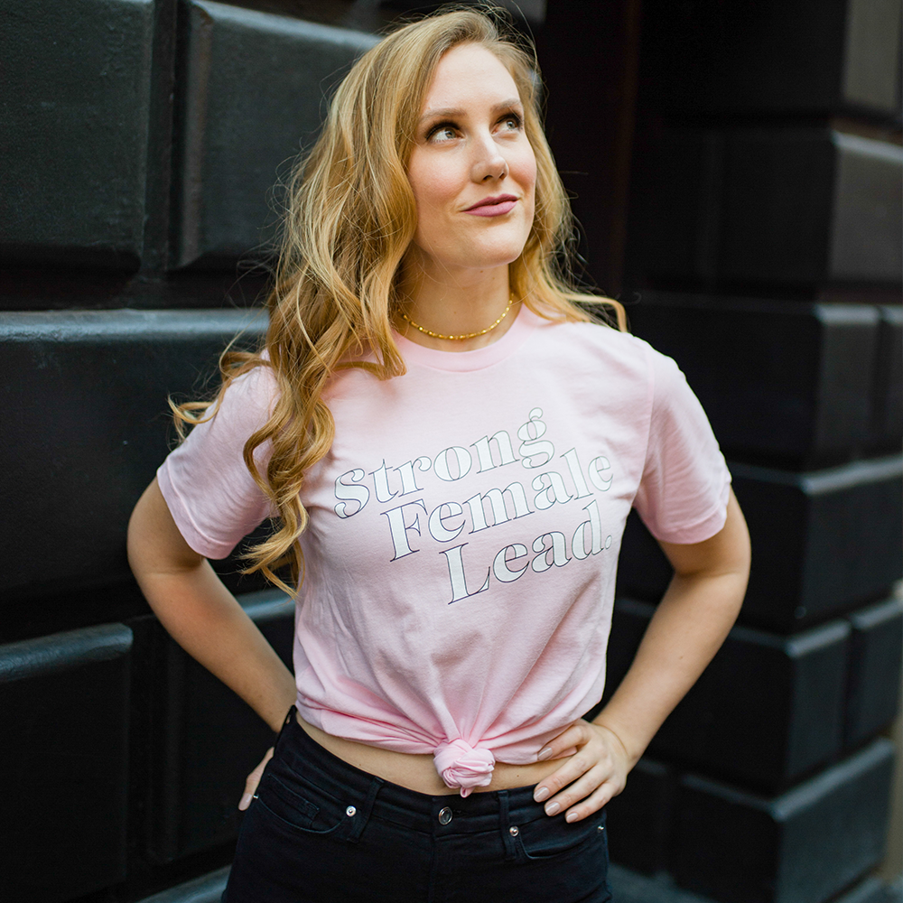 Model wearing a pink t-shirt with the words &quot;Strong Female Lead&quot; written in white
