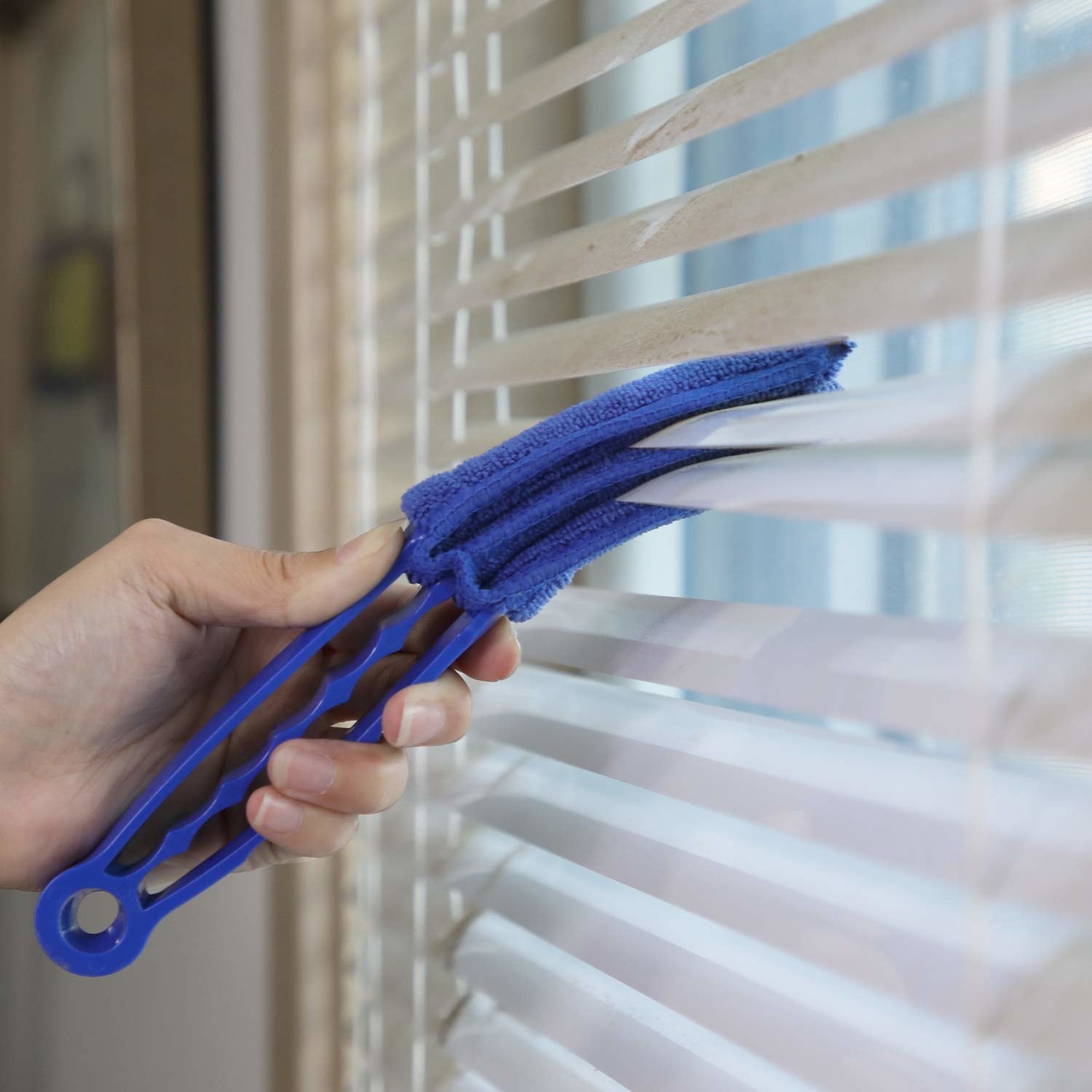 A hand using the three-pronged tool — with each part covered in microfiber — to reach in between blinds