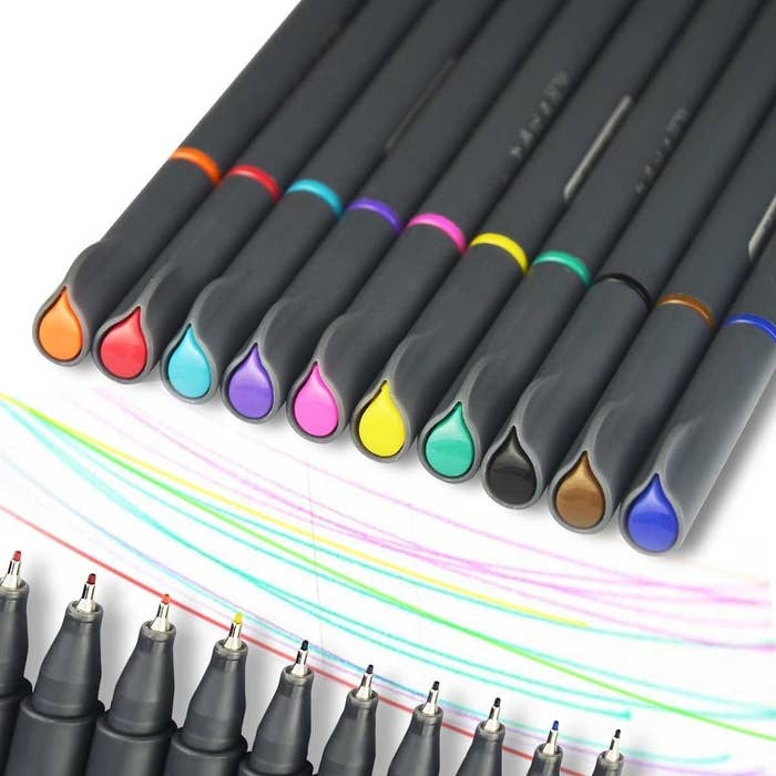 Ten fine-point pens lying on a sheet of paper with different coloured lines beside them
