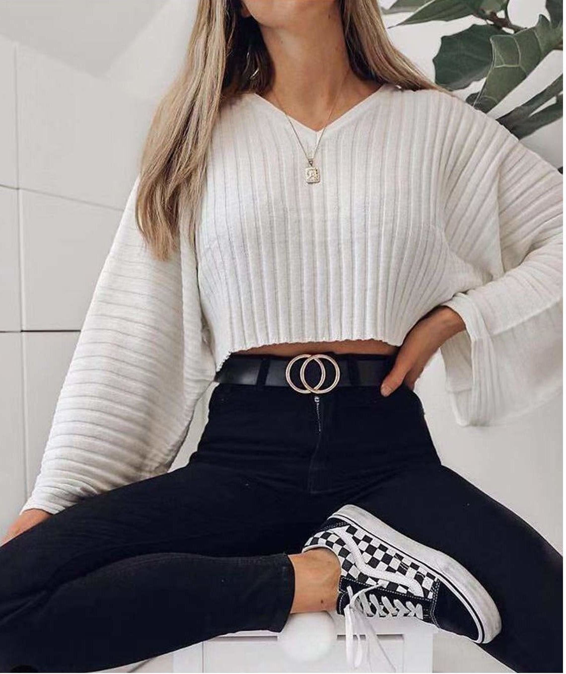 A person siting with their hand on their hip They are wearing a long sleeved shirt, jeans, and a belt with a buckle in the shape of two interlocked circles