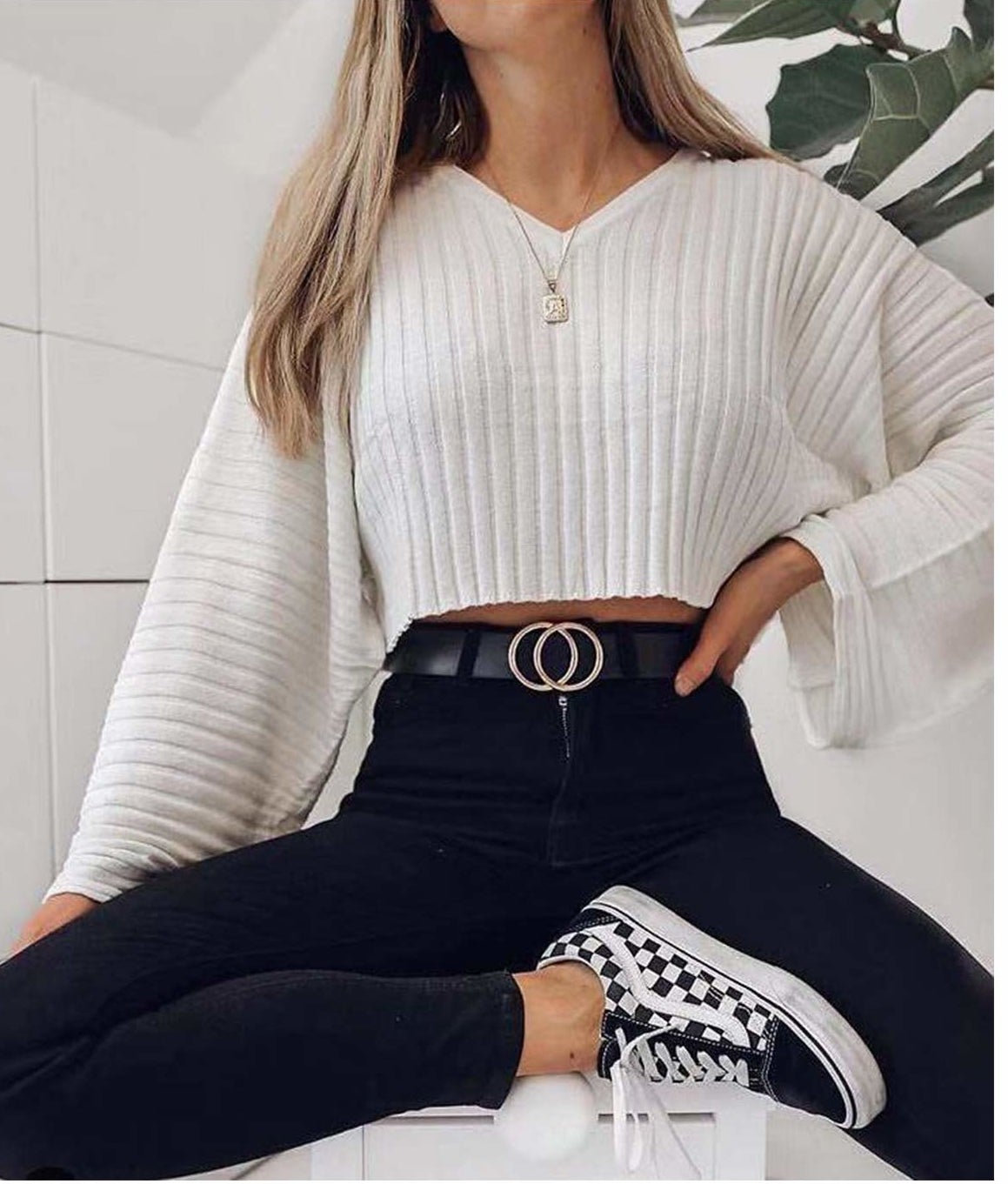 A person sitting with their hand on their hip They are wearing a long sleeved shirt, jeans, and a belt with a buckle in the shape of two interlocked circles