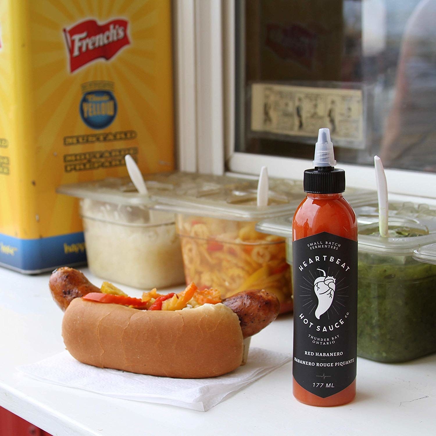 A bottle of the hot sauce next to a hot dog