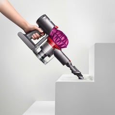 A hand holding the handheld vacuum with nozzle to clean dust off steps