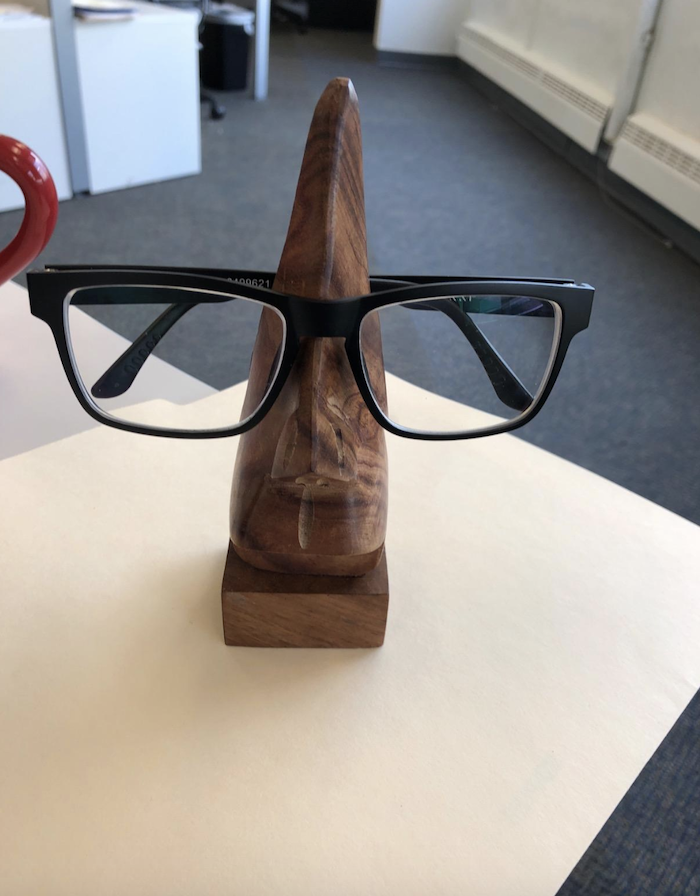 a reviewer's glasses sitting on the holder which is a wooden sculpture of a nose