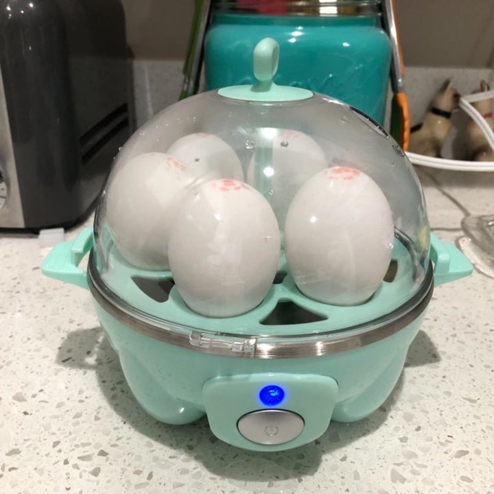 A reviewer showing the dome-shaped cooker in light blue with five eggs inside 