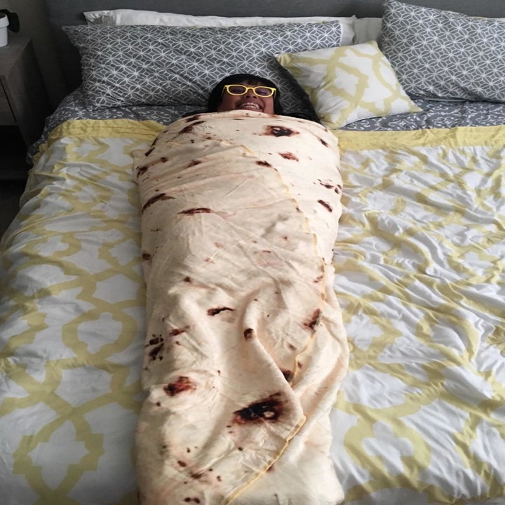 A reviewer laying on a bed wrapped up in the blanket, looking like a human burrito