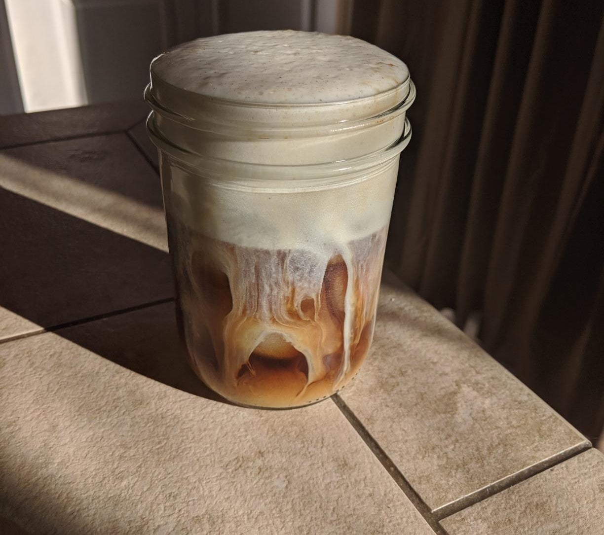 A mason jar with iced coffee and thick foam
