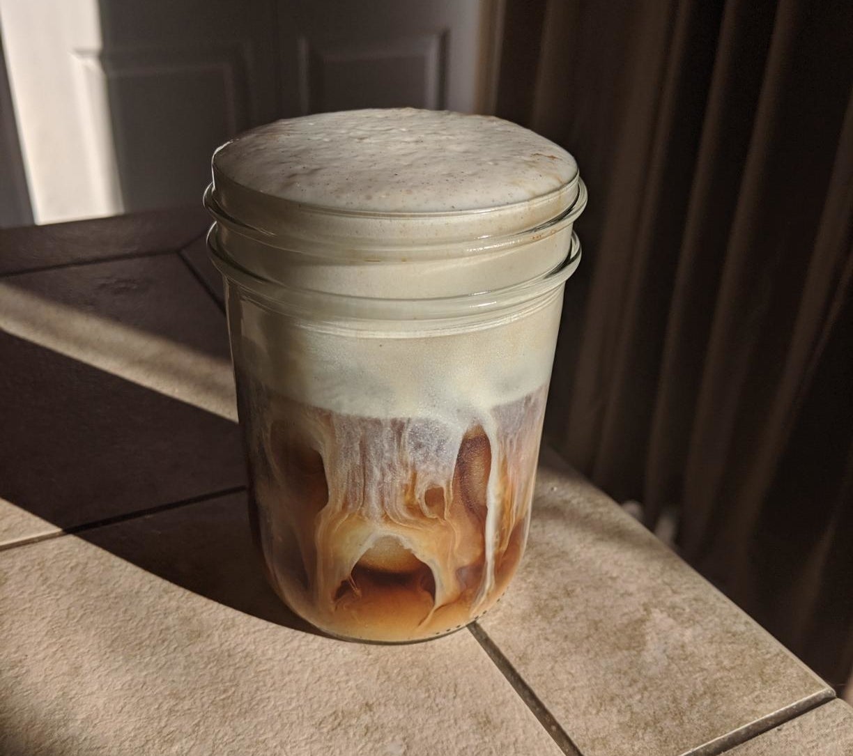 a mason jar with iced coffee and thick foam