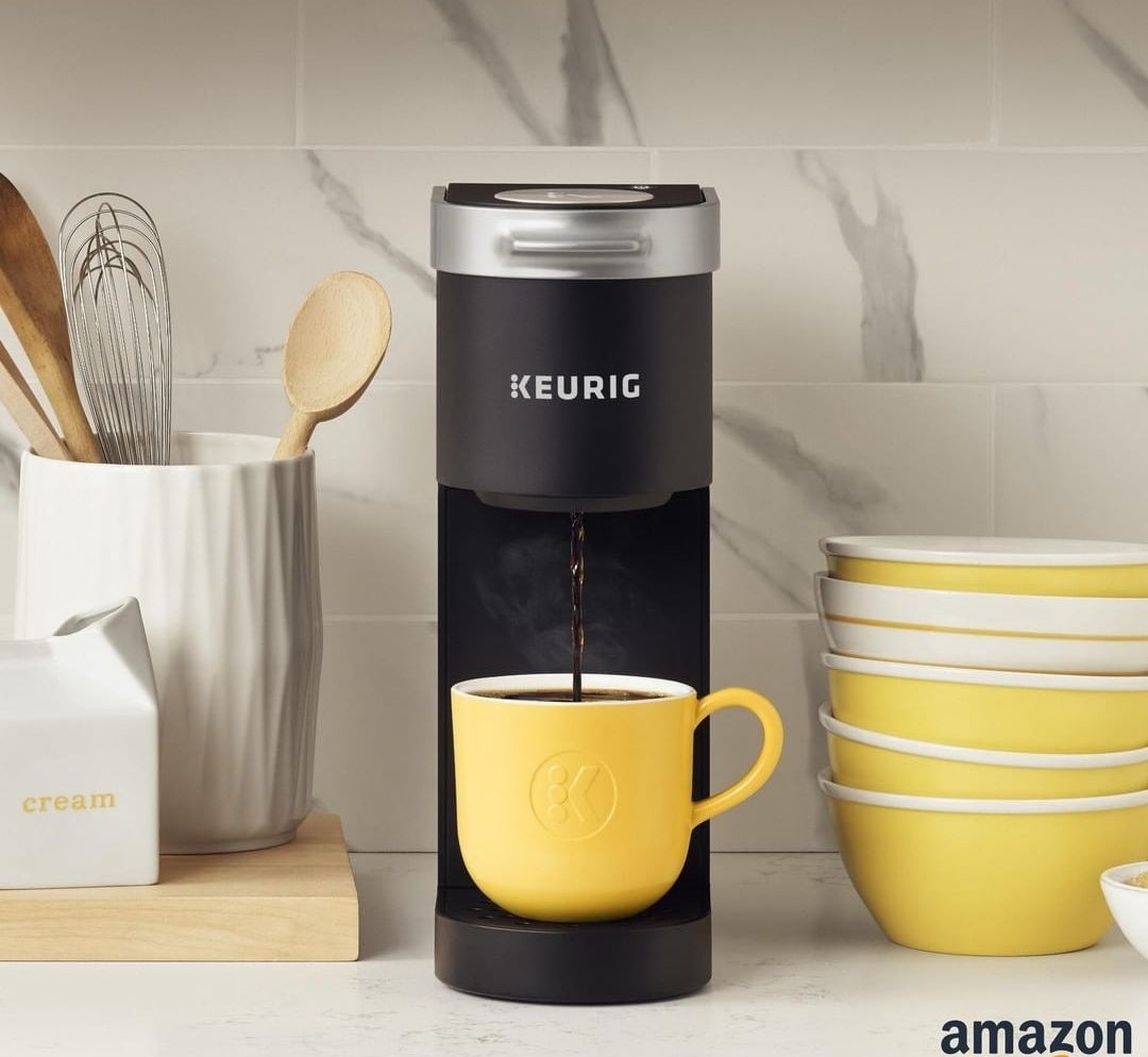 A small coffee maker on a counter dispensing coffee into a mug