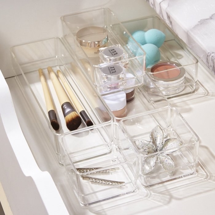 the vanity trays in square and rectangle shapes. They&#x27;re made of clear acrylic and holding jewelry, bejeweled tweezers, makeup brushes and more