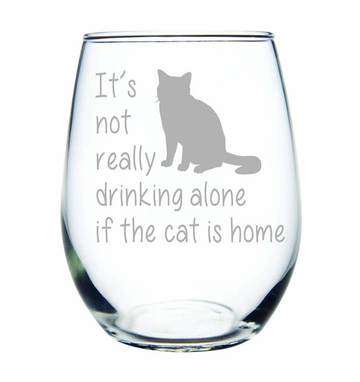 a stemless wine glass with a cat on it that says &quot;it&#x27;s not really drinking alone if the cat is home&quot; 