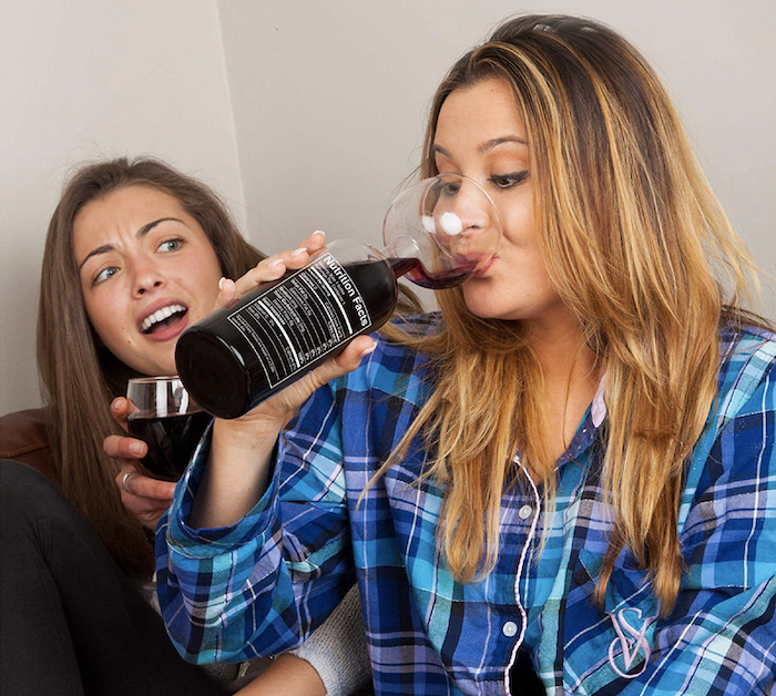 model drinking from the bottomless wine glass which is shaped like an actual wine bottle at the bottom except the "neck" of the bottle is actually the "stem" of its wine glass top