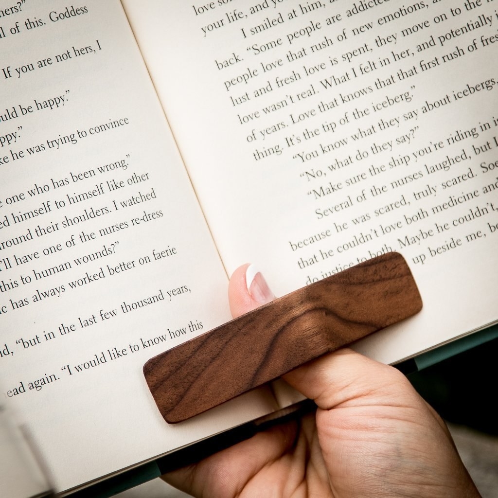 A thumb looped into a rectangular wooden page holder keeping a book open 